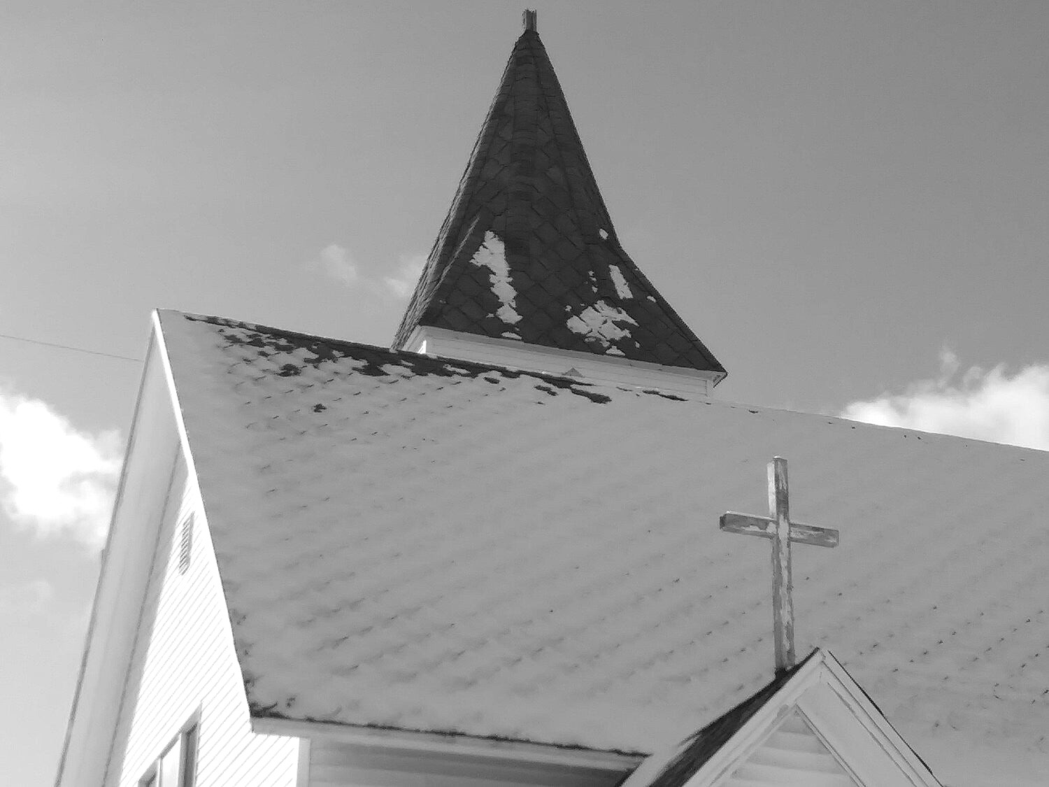 The chapel steeple and roof cross under snow against a clear sky