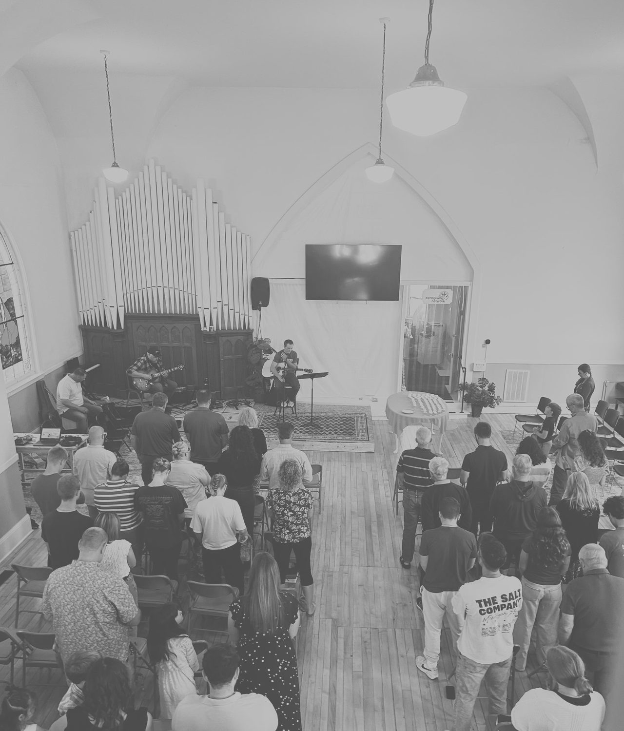 The congregation standing together during Sunday worship, seen from the balcony, with the pipe organ and the band at the front of the sanctuary